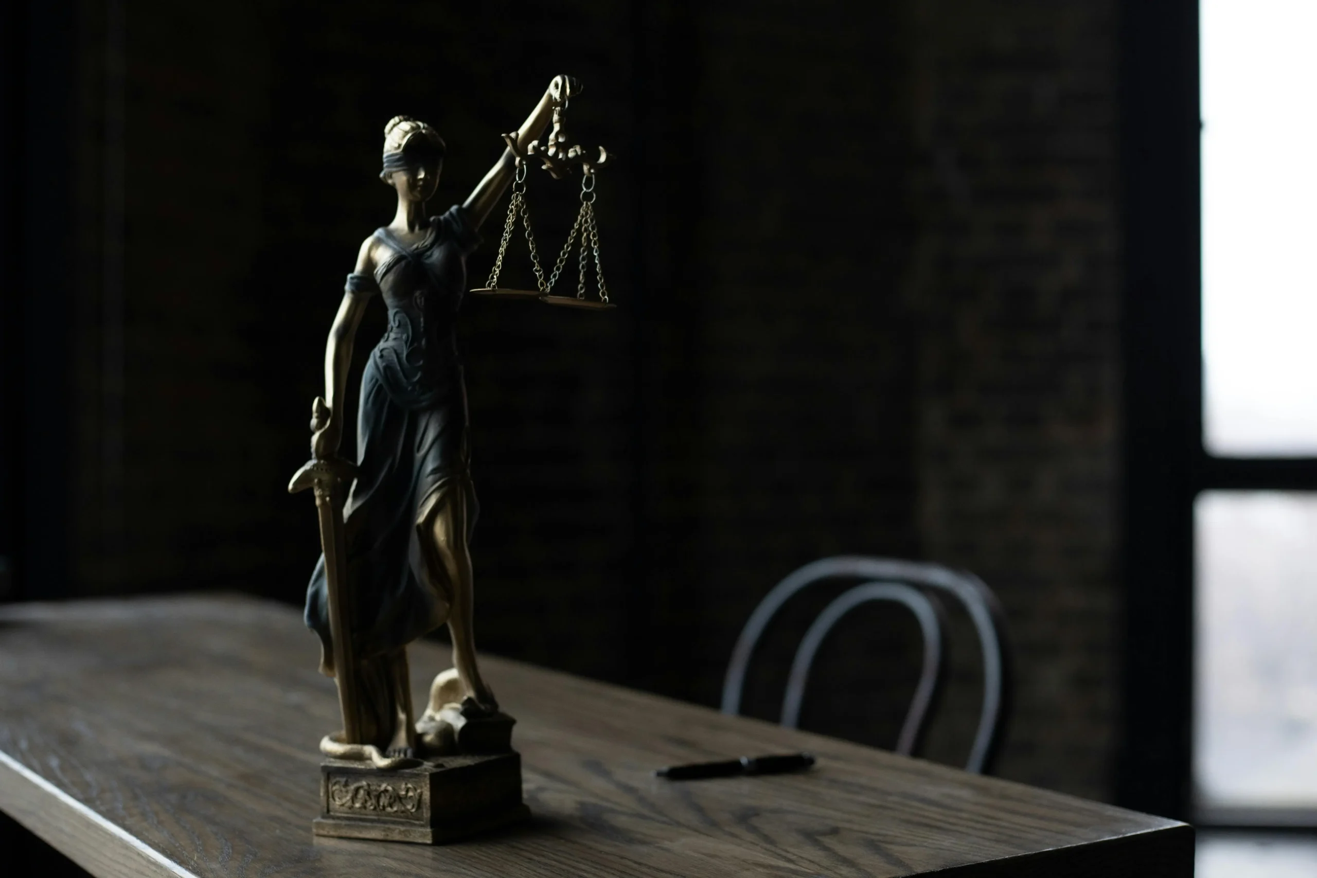 A statue of Lady Justice holding scales and a sword, positioned on a wooden table in a dimly lit room.